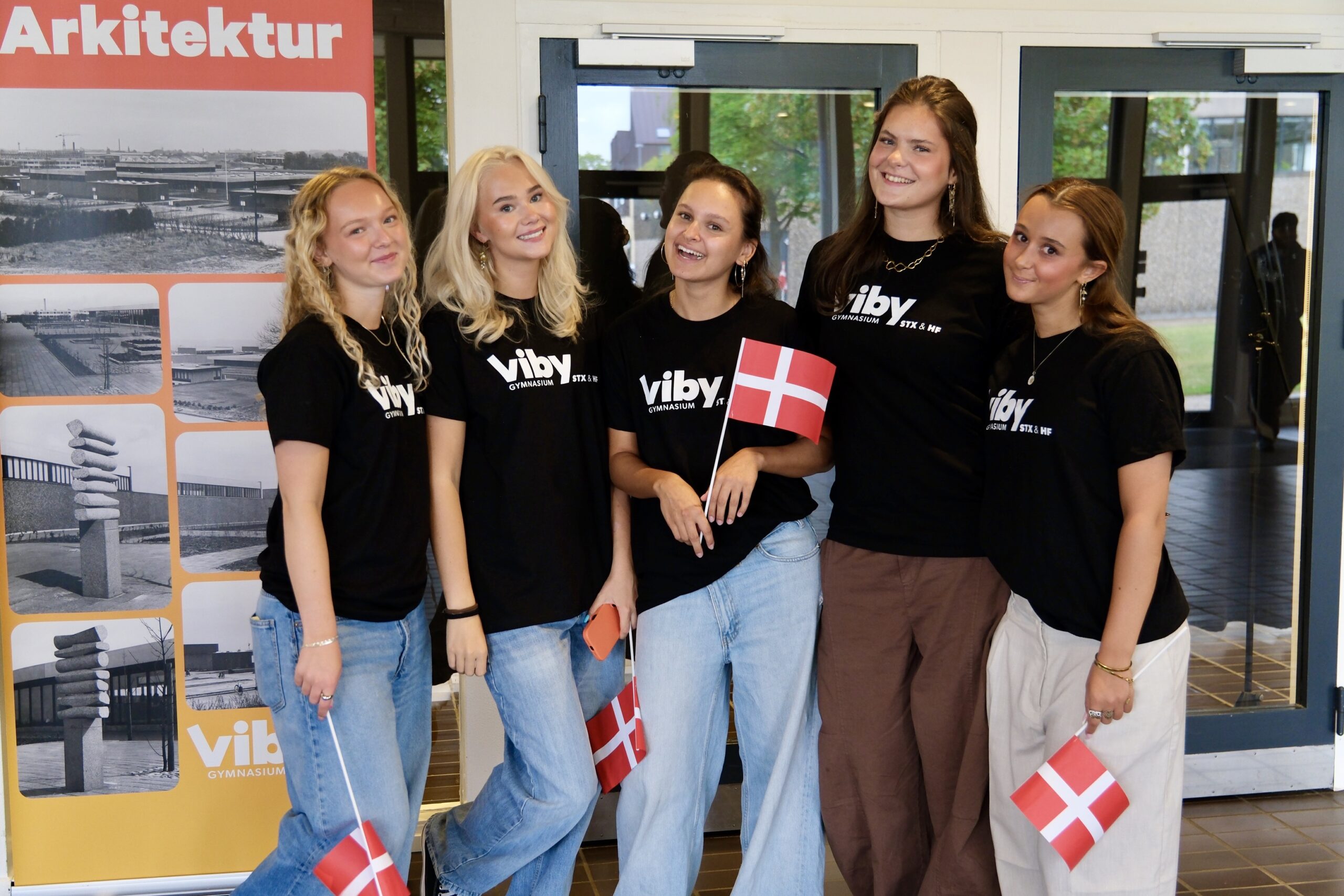 Fem unge kvinder fra Viby Gymnasium smiler og holder små danske flag.