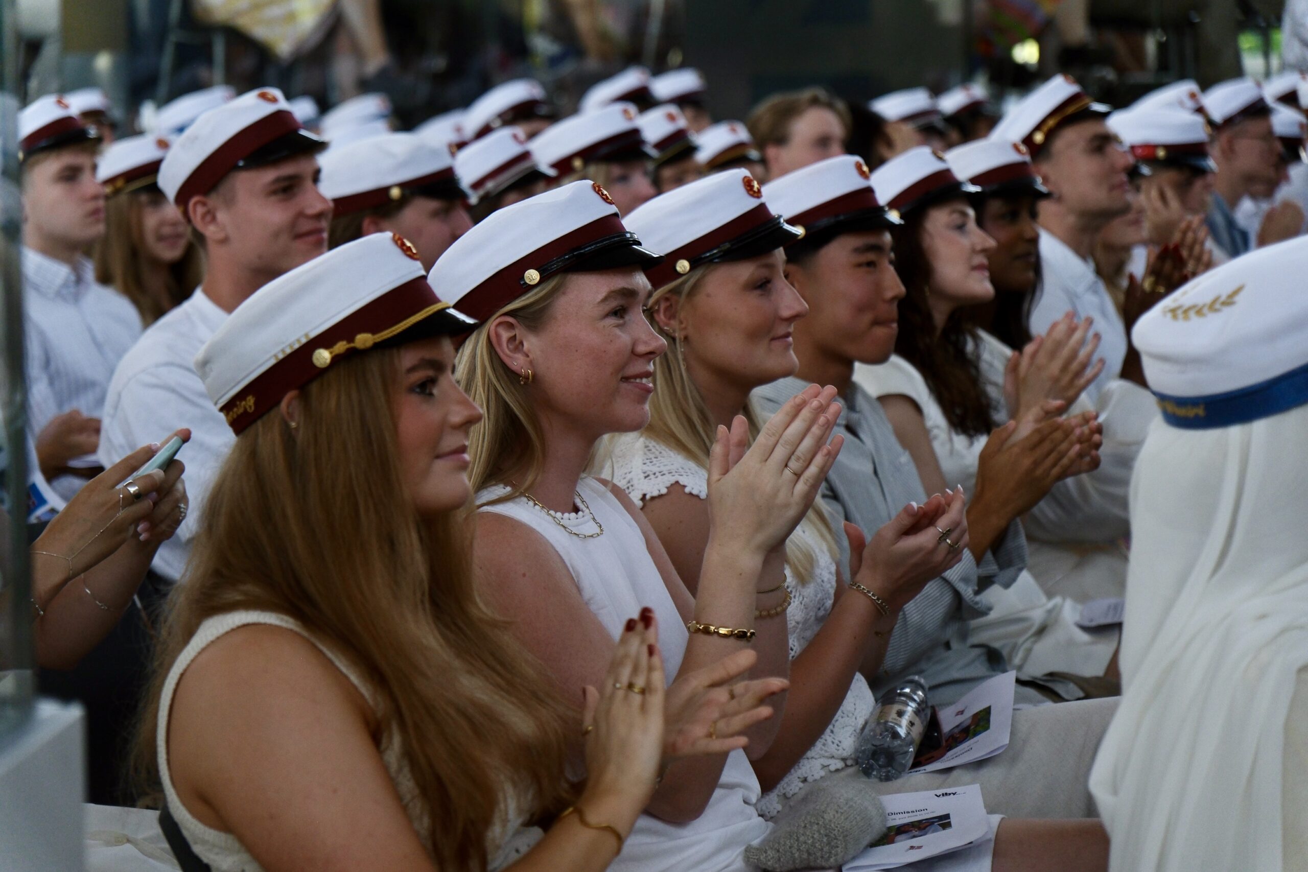 Glade studenter i studenterhuer klapper under en ceremoni efter endt gymnasial uddannelse.